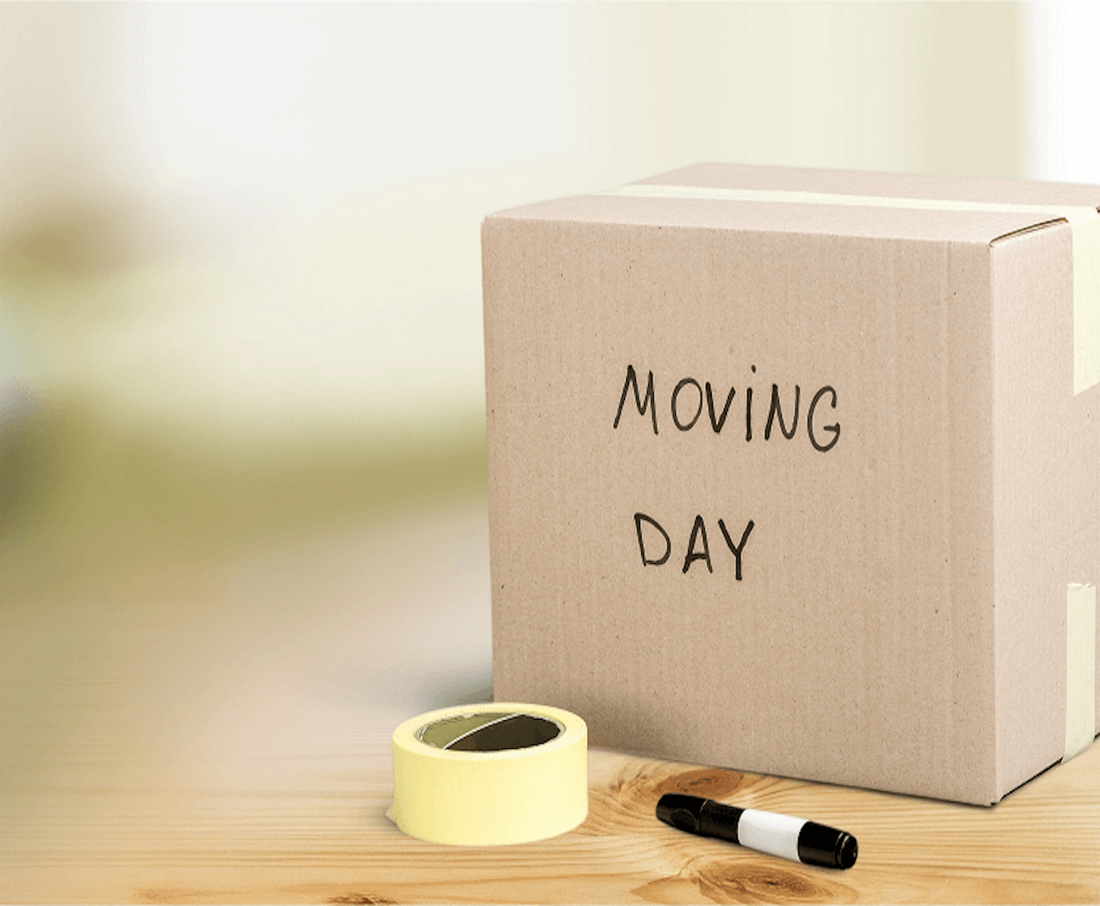 A cardboard box labeled 'Moving Day' with yellow packing tape and a black marker on a wooden table, symbolizing safe relocation preparation.
