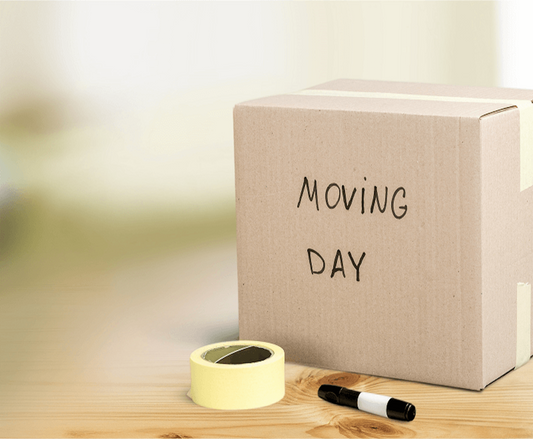 A cardboard box labeled 'Moving Day' with yellow packing tape and a black marker on a wooden table, symbolizing safe relocation preparation.